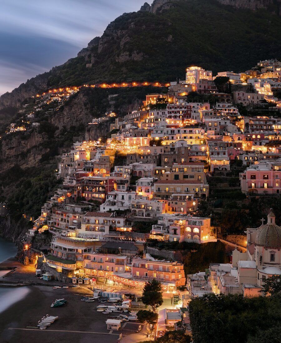 Positano at dusk — lit houses stacked down the Amalfi Coast cliffside to the sea