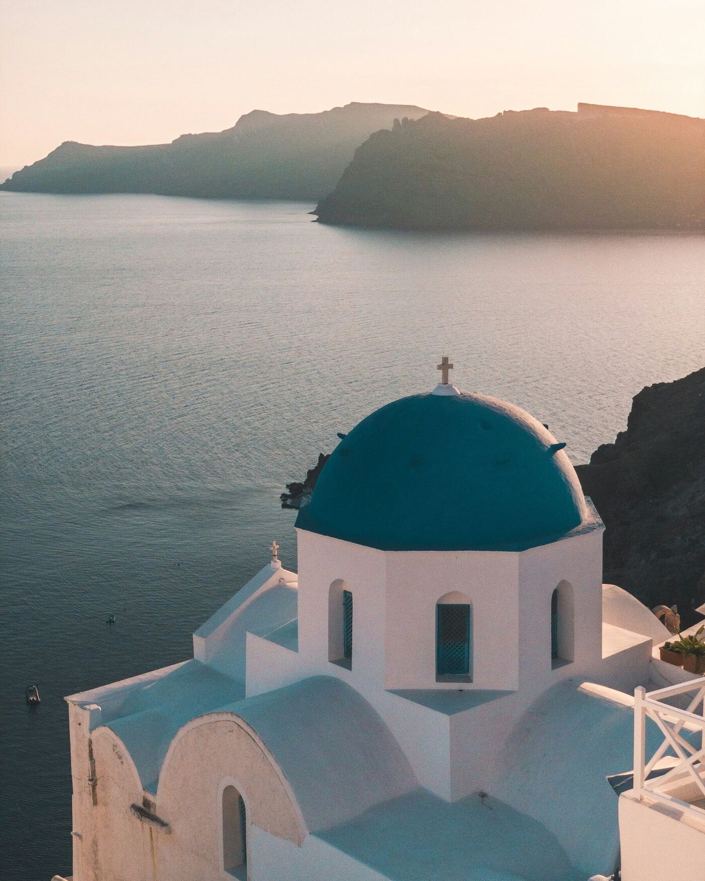 Blue-domed church above the Aegean caldera at sunset in Santorini